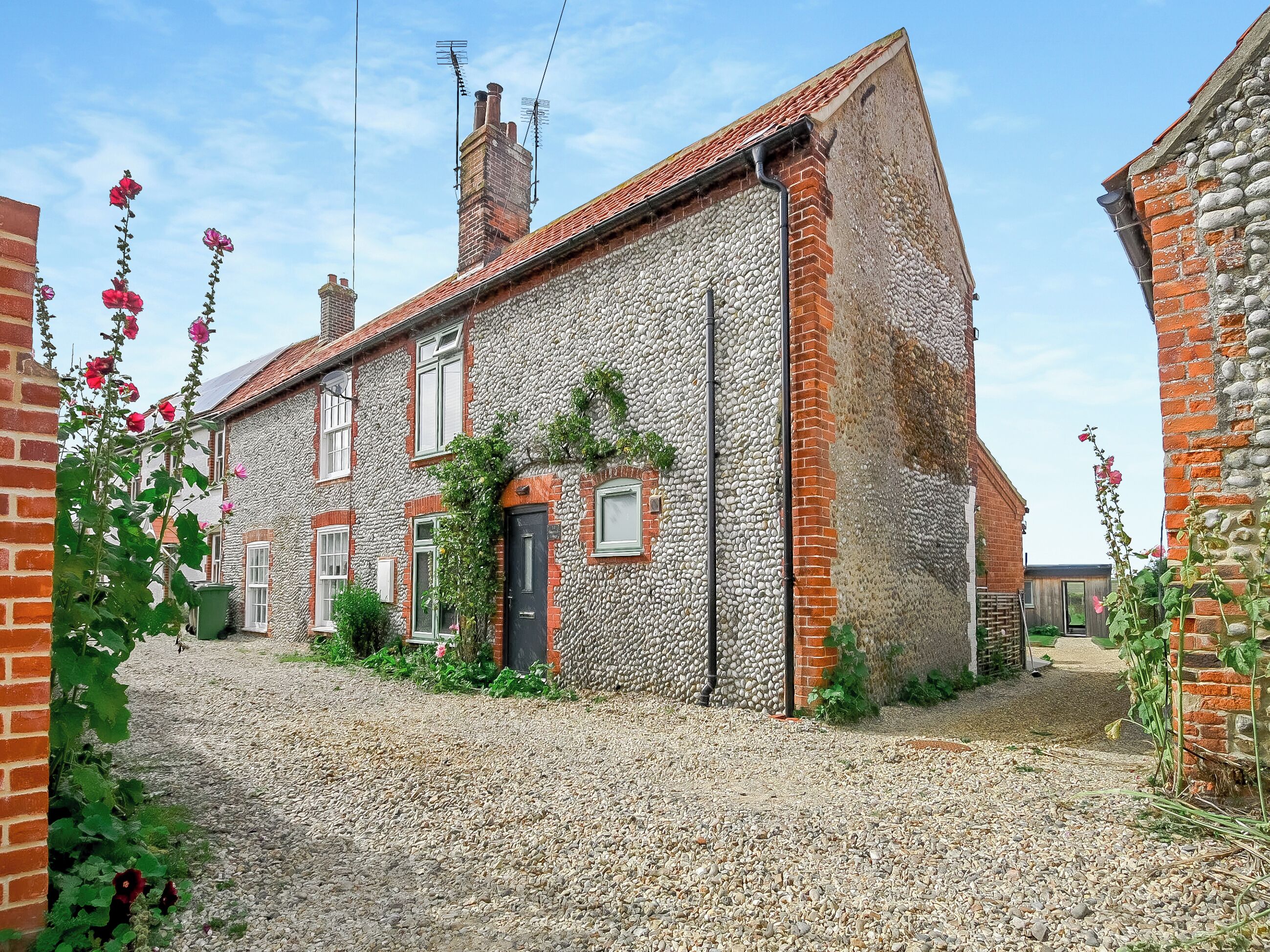 A traditional stone house with a gravel driveway, a black door, and a chimney.