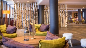 A lobby with a wooden coffee table, colorful cushions, a decorative tree, and a Christmas tree in the background.