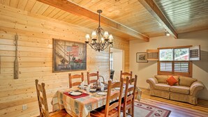 A cozy wooden cabin interior with a dining table set for four, wooden chairs, a chandelier, and a sofa with a window view. - Cabin w/ Backyard Space - 1/2 Mi to Trinity Lake! (Trinity Center)