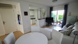 A modern living room with a white couch, a round dining table, and a kitchen in the background.
