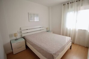 A bedroom with a bed, bedside tables, a lamp, a picture on the wall, and a window with curtains.