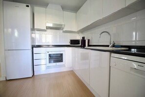 Een moderne keuken met witte kasten, een magnetron, een inbouwoven, een Bosch vaatwasser en een roestvrijstalen spoelbak.