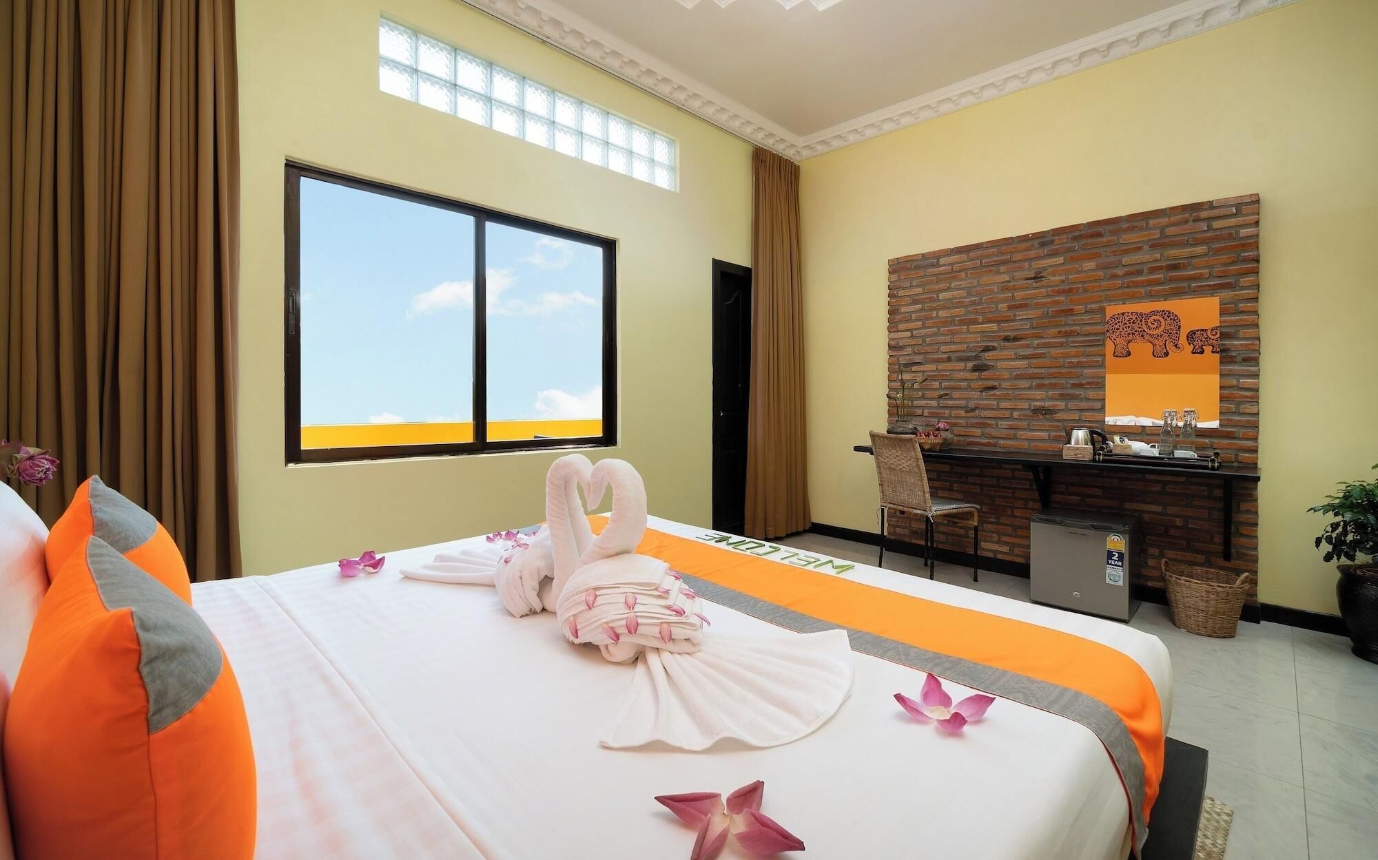 A hotel room with a bed, a desk, a chair, a window, a brick wall, and a ceiling with a skylight.