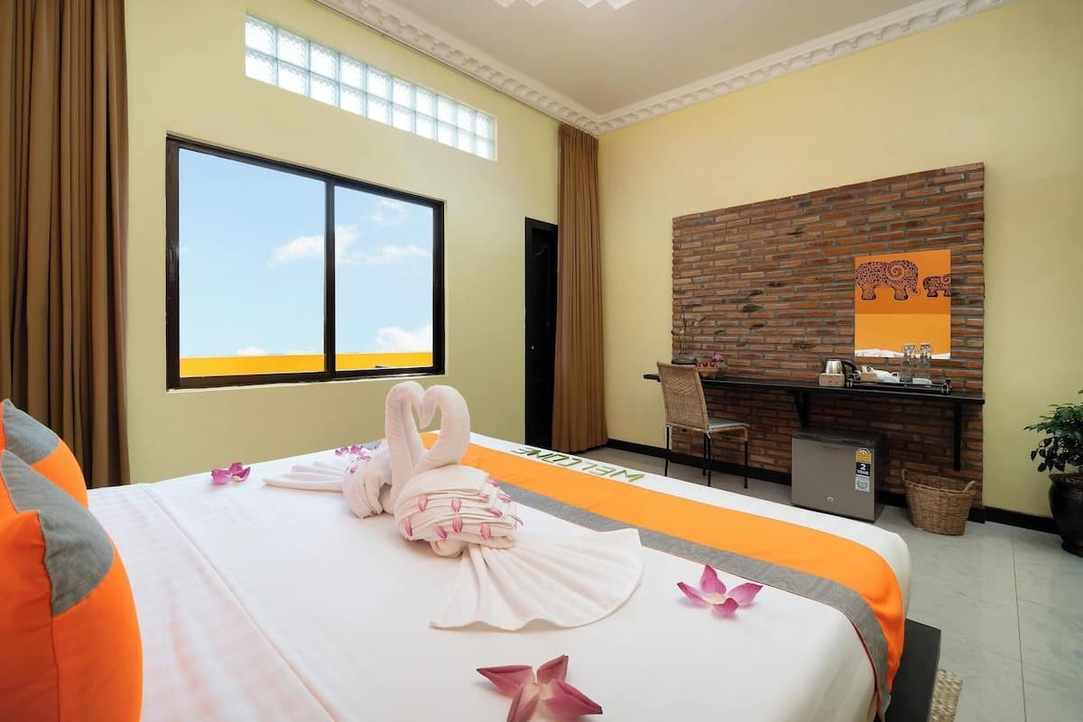 A hotel room with a bed, a desk, a chair, a window, a brick wall, and a ceiling with a skylight.