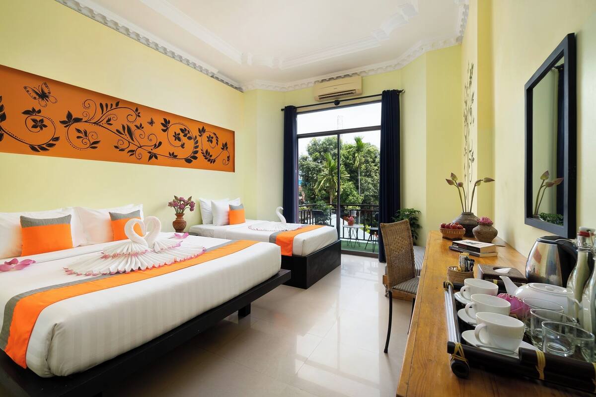 A hotel room with two beds, a balcony with a view, a dining area with tableware, and a wall with a floral design.