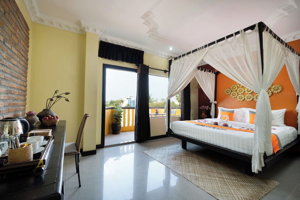 A four-poster bed with a canopy, a dining table with chairs, a potted plant, and a view of the outdoors.