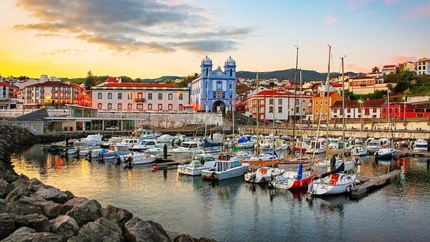 Un puerto con barcos amarrados, una iglesia azul destacada y edificios a lo largo del paseo marítimo.