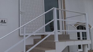 Un edificio con fachada blanca, un letrero que dice "AL" y una escalera que conduce a una ventana con contraventanas.