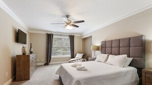 A bedroom with a large bed, a ceiling fan, a TV, a dresser, and a window with curtains. - Beautiful Atlanta Home Sleeps Up to 20 (Ellenwood)