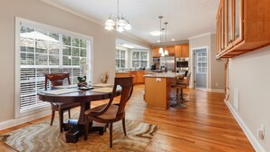 A spacious kitchen with wooden cabinets, a central island, and a dining area with a round table and chairs. - Beautiful Atlanta Home Sleeps Up to 20 (Ellenwood)