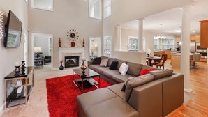 A spacious living room with a fireplace, a large sofa, and a red rug. - Beautiful Atlanta Home Sleeps Up to 20 (Ellenwood)