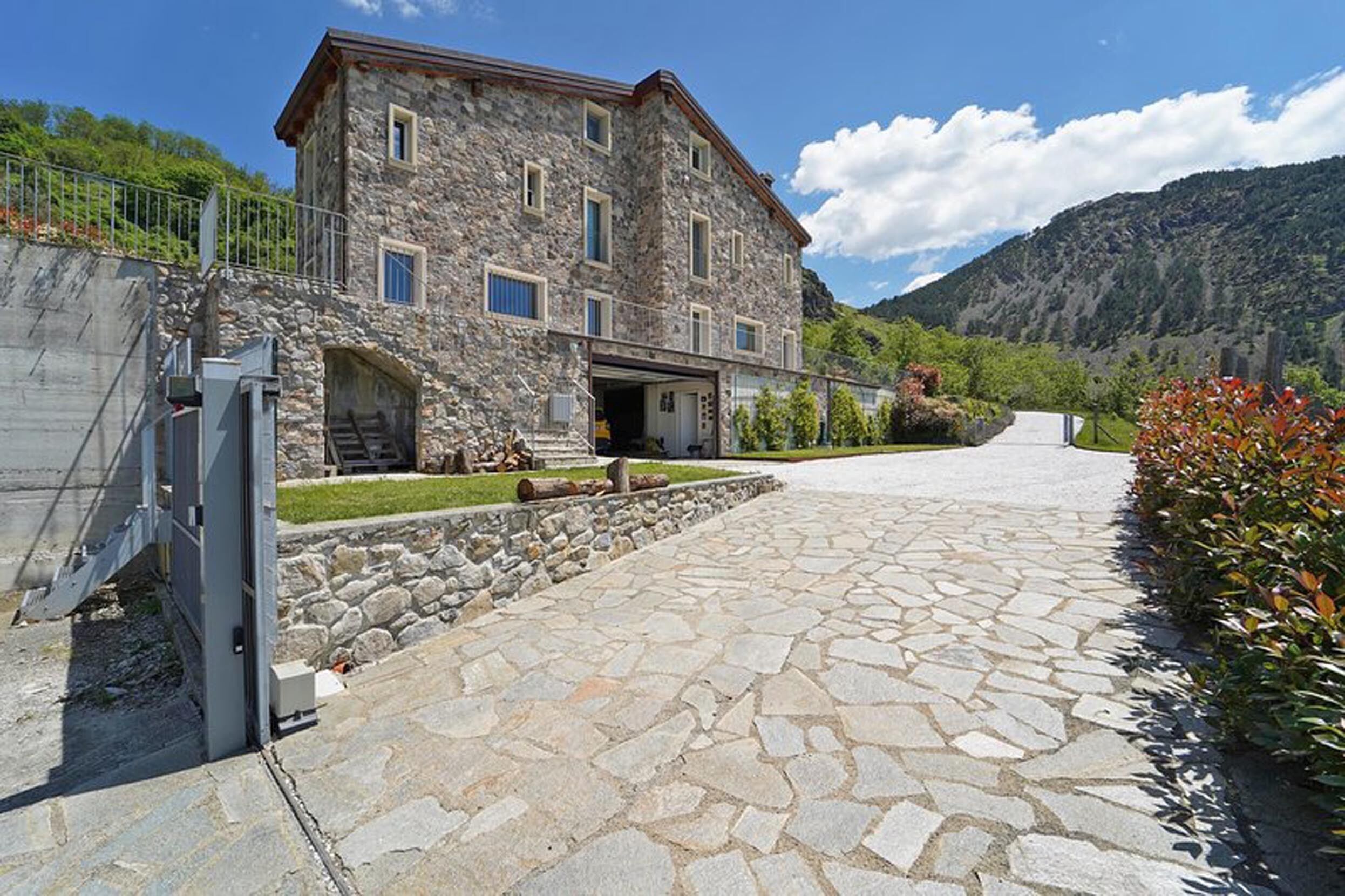 Un edificio in pietra con una scalinata in pietra, un vialetto lastricato e montagne sullo sfondo.