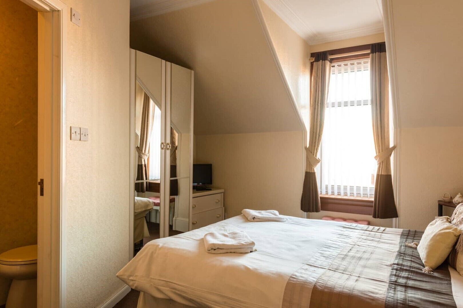 A bedroom with a bed, a television, a wardrobe, and a window with curtains.