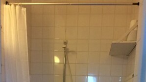 Une petite salle de bain carrelée, équipée de toilettes, d’une douche et d’un lavabo.
