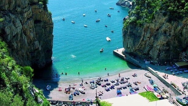 A coastal beach with boats, cliffs, and a paved area with umbrellas and lounge chairs. - VILLA LUCE - Five Bedroom Villa, Sleeps 10 (Praiano)