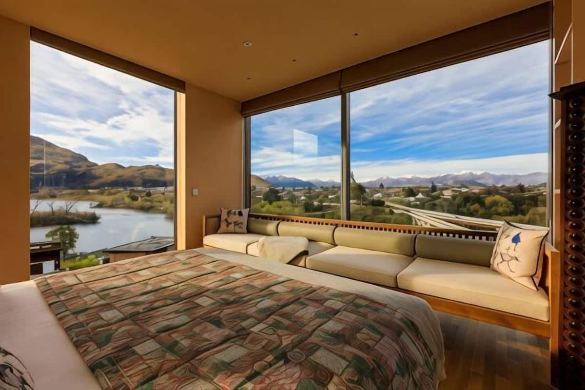 A bedroom with a large bed, a sofa, and a view of a lake and mountains.