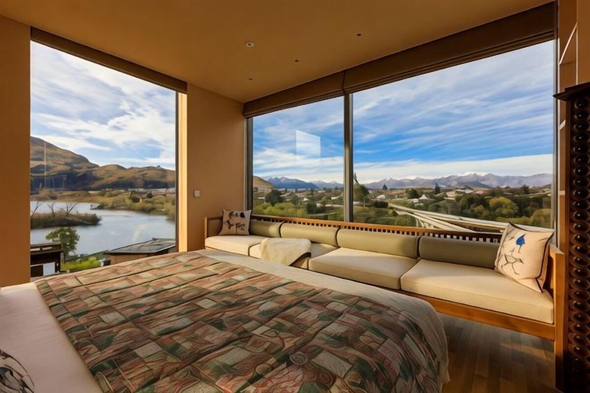 A bedroom with a large bed, a sofa, and a view of a lake and mountains.