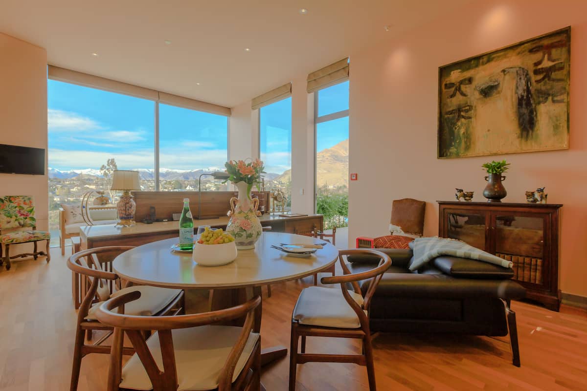 A spacious living room with a large dining table, comfortable seating, and a view of mountains through large windows.