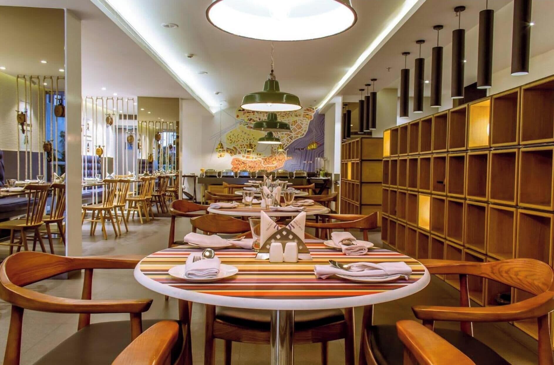 A restaurant interior with round tables, wooden chairs, and a modern chandelier.