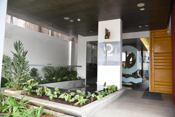 A modern hotel entrance with a reception desk, a sign for 'The Port Hotel', and a landscaped area with plants.