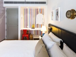 Habitación de hotel con cama, escritorio, silla, lámpara y un reloj en la pared.