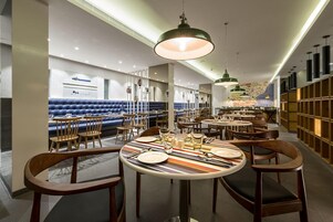 Un interior de restaurante moderno con mesas redondas, asientos acolchados azules e iluminación colgante.