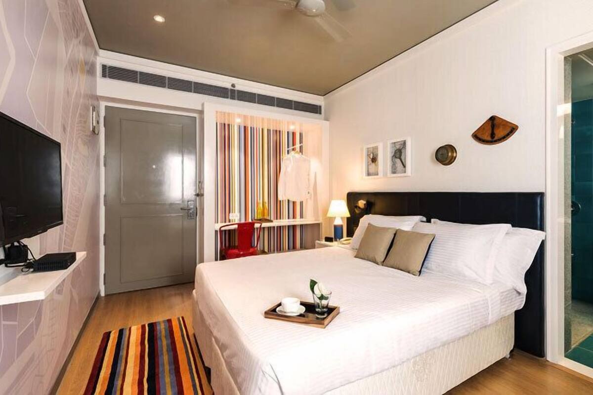 Une chambre d’hôtel avec un lit, une télévision, un bureau avec un ordinateur, une bibliothèque et une salle de bain visible à travers une porte ouverte.