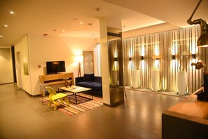 A modern living room with a sofa, a coffee table, and a TV. There is a striped rug on the floor. - The Port Hotel (Visakhapatnam)