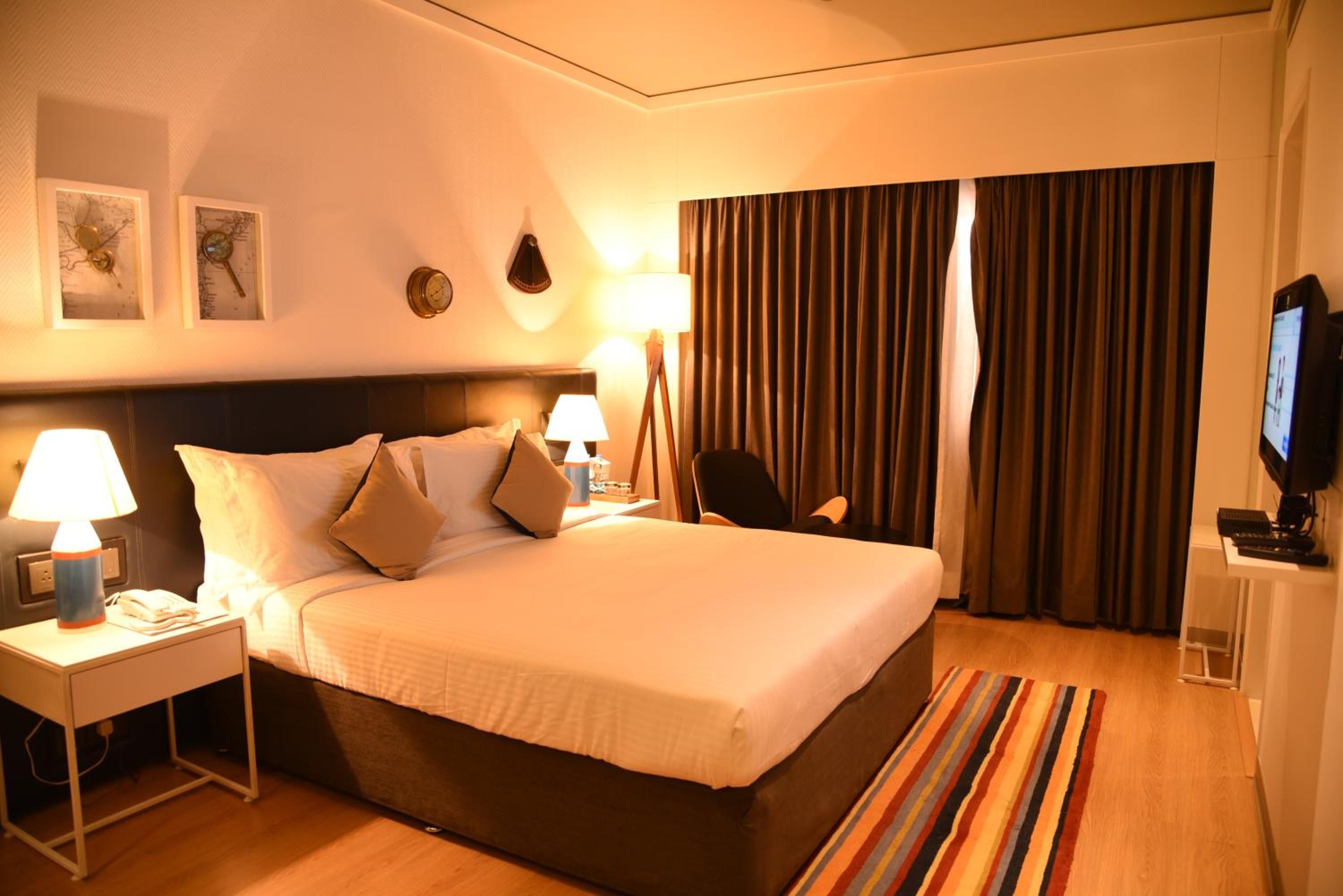 Een hotelkamer met een groot bed, twee bedlampen, een bureau met een computer en een televisie.