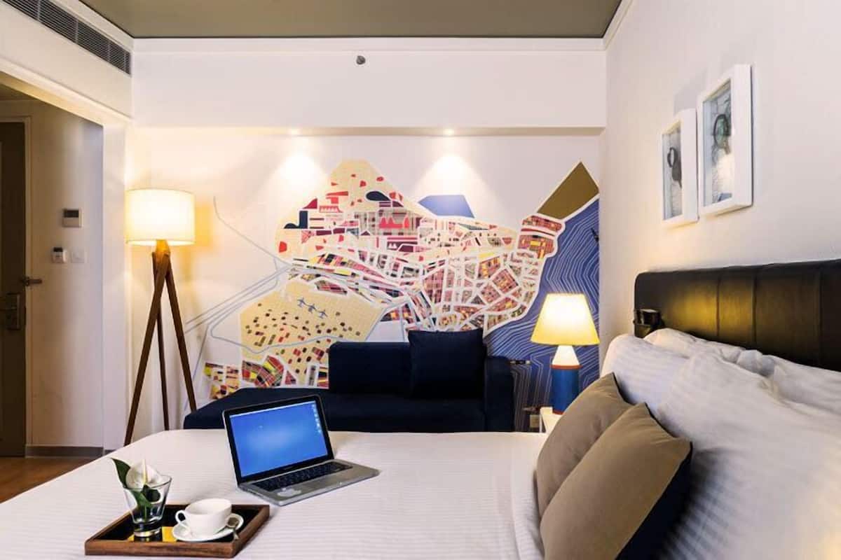 Une chambre d’hôtel avec un lit, un bureau avec un ordinateur portable, une carte accrochée au mur et deux lampes.