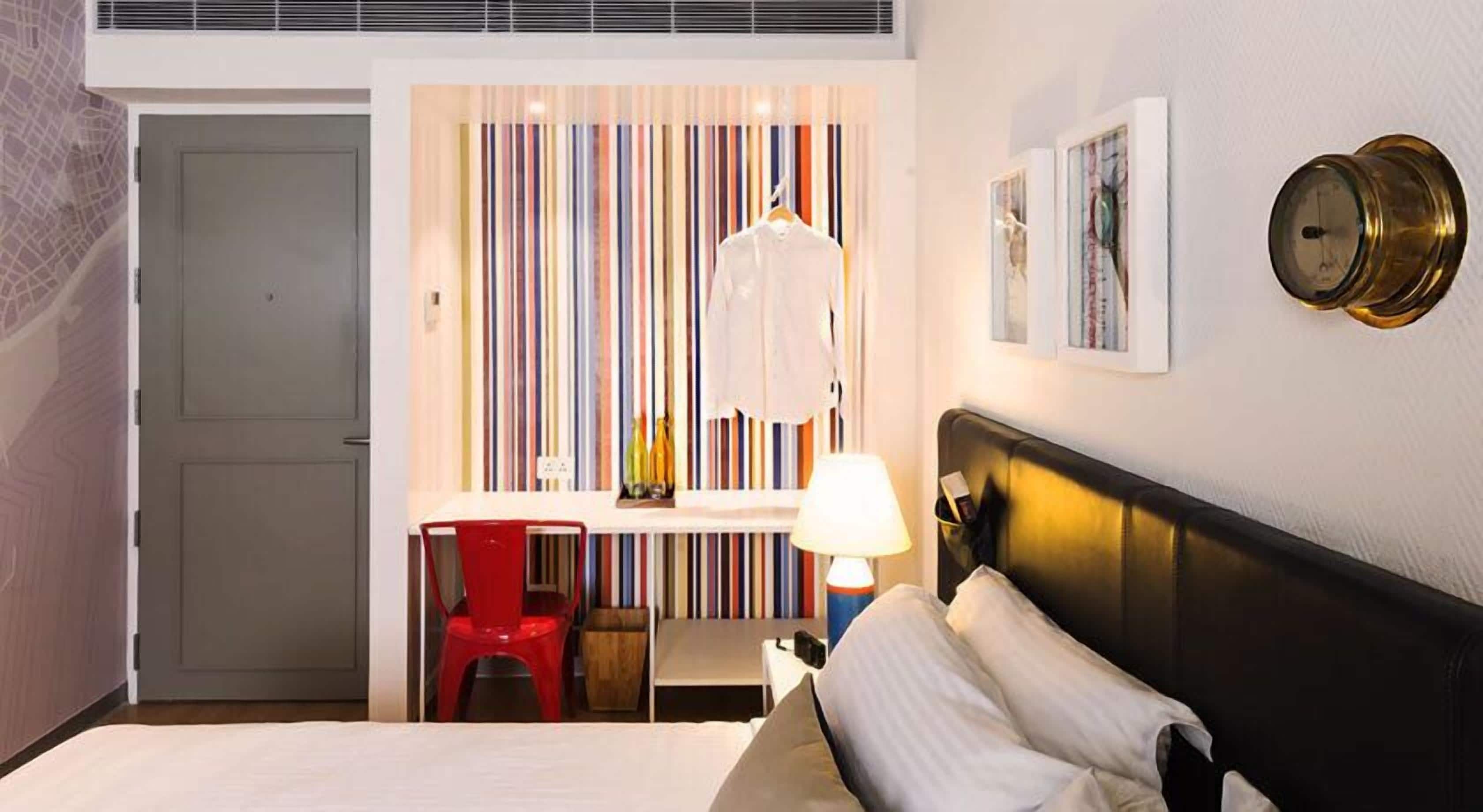 Ein Hotelzimmer mit Bett, Schreibtisch mit Stuhl, Lampe und Wand mit Streifenmuster.