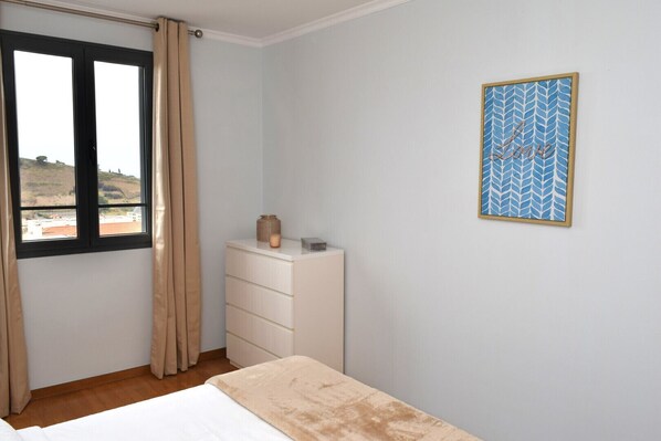 A bedroom with a bed, a dresser, a window with curtains, and a wall-mounted picture.