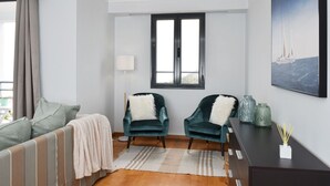 A modern room with a bed, two chairs, a desk, and a window.