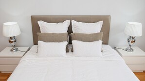 A neatly made bed with white linens, a beige headboard, and two bedside tables with lamps.
