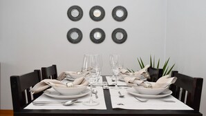 A dining table set with white plates, bowls, and cutlery, flanked by black chairs.