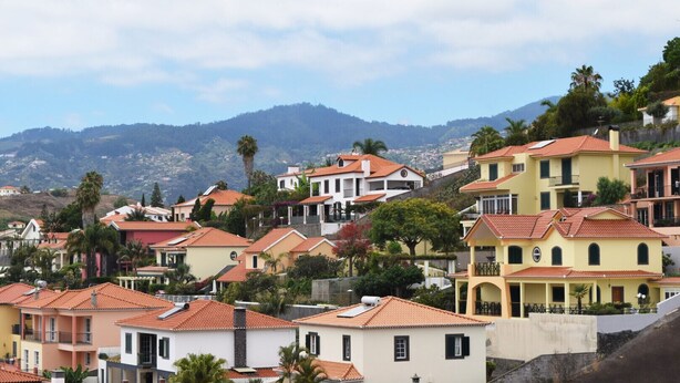 A hillside residential area with colorful houses, some with balconies, and a mountainous backdrop.