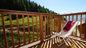 Eine Holzterrasse mit einem Stuhl und einem Getränk, mit Blick auf eine grüne Landschaft und entfernte Berge.