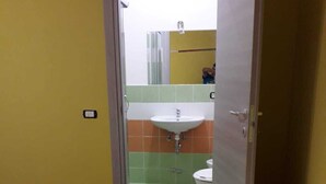 A bathroom with a sink, toilet, and shower. There is a wooden floor and a door leading to another room.