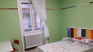 A small, brightly colored room with a single bed, a desk, and a chair.