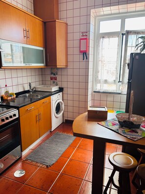 A kitchen with wooden cabinets, a washing machine, a sink, and a window with curtains. - GARDEN VIEW APARTMENT (HORTA)