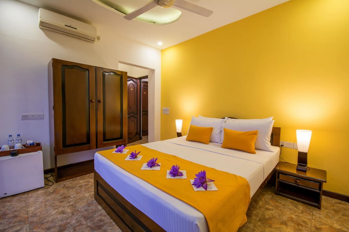 A hotel room with a bed, bedside lamps, a nightstand, a wardrobe, and an air conditioning unit.