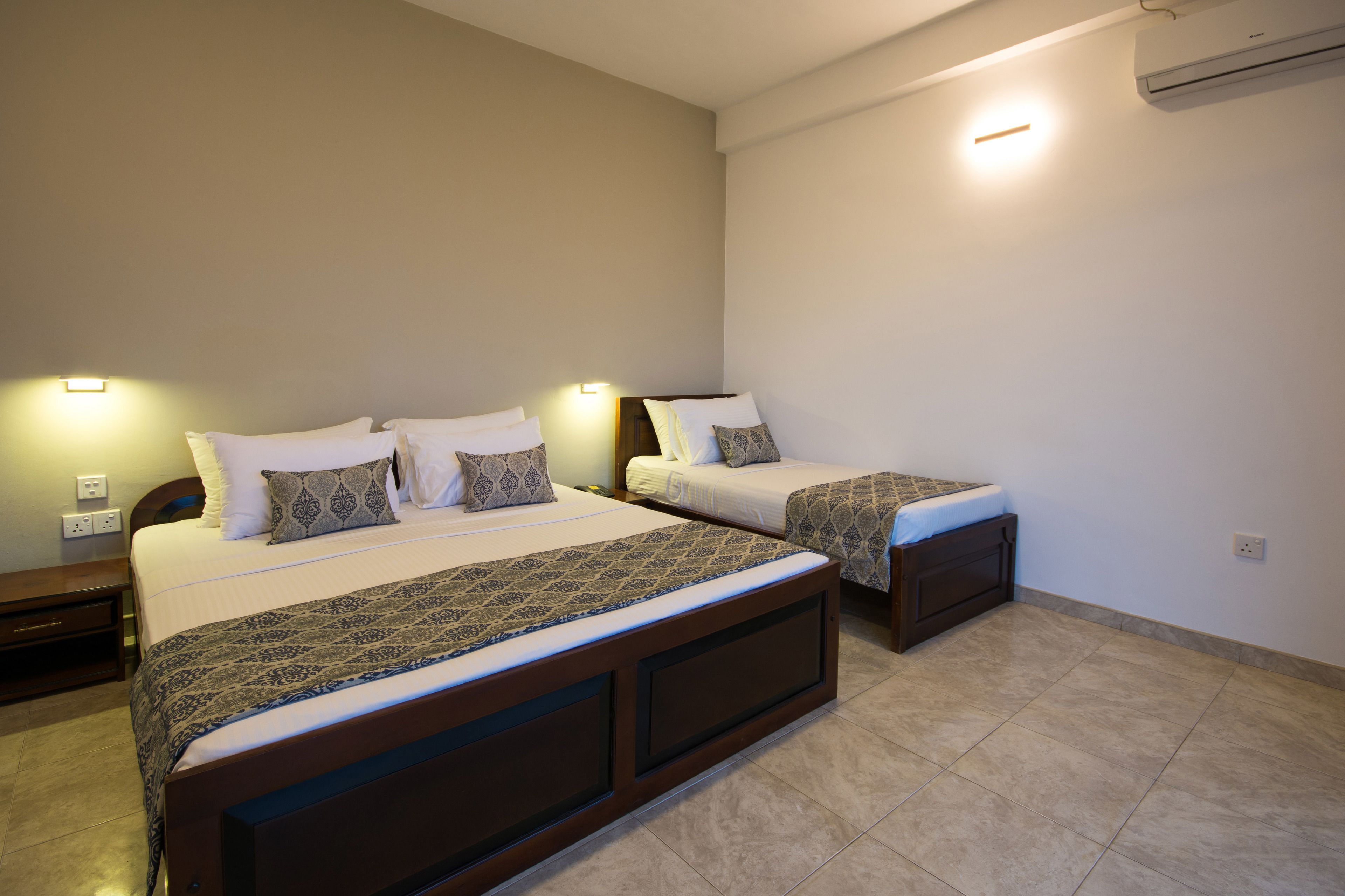 A hotel room with two single beds, a wooden headboard, a nightstand, and a wall-mounted air conditioner.