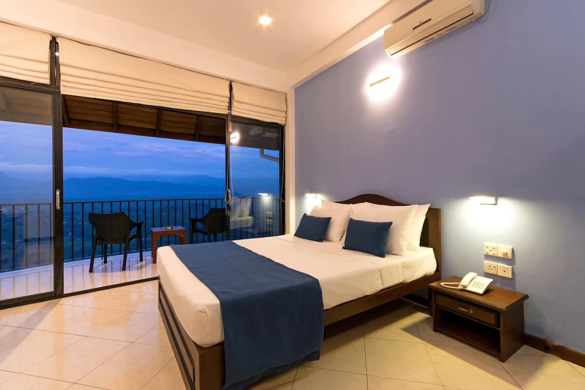 A hotel room with a bed, bedside table, and a phone. There is a balcony with a chair and a table.