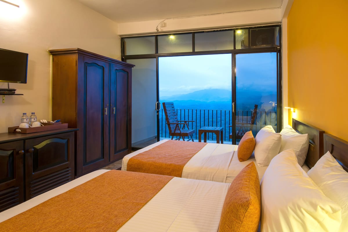 A hotel room with two beds, a TV, a wardrobe, and a balcony with a view of the mountains.