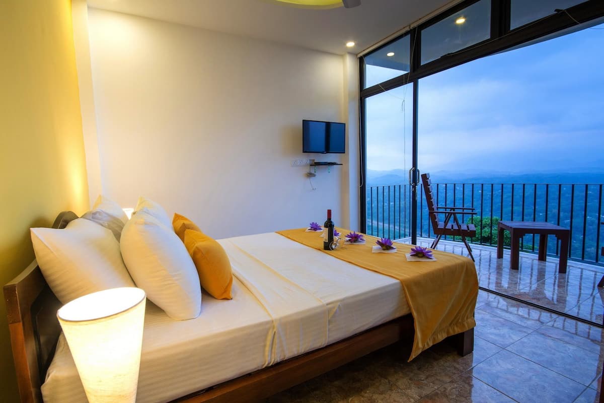 A bedroom with a bed, a TV, and a balcony with a view.