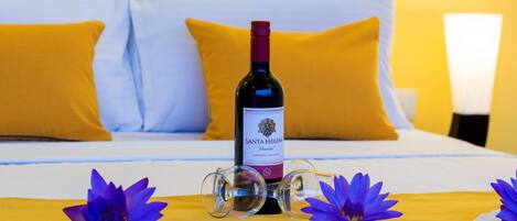 A bed with yellow pillows, a bottle of Santa Helena wine, and purple flowers on a yellow bedspread.