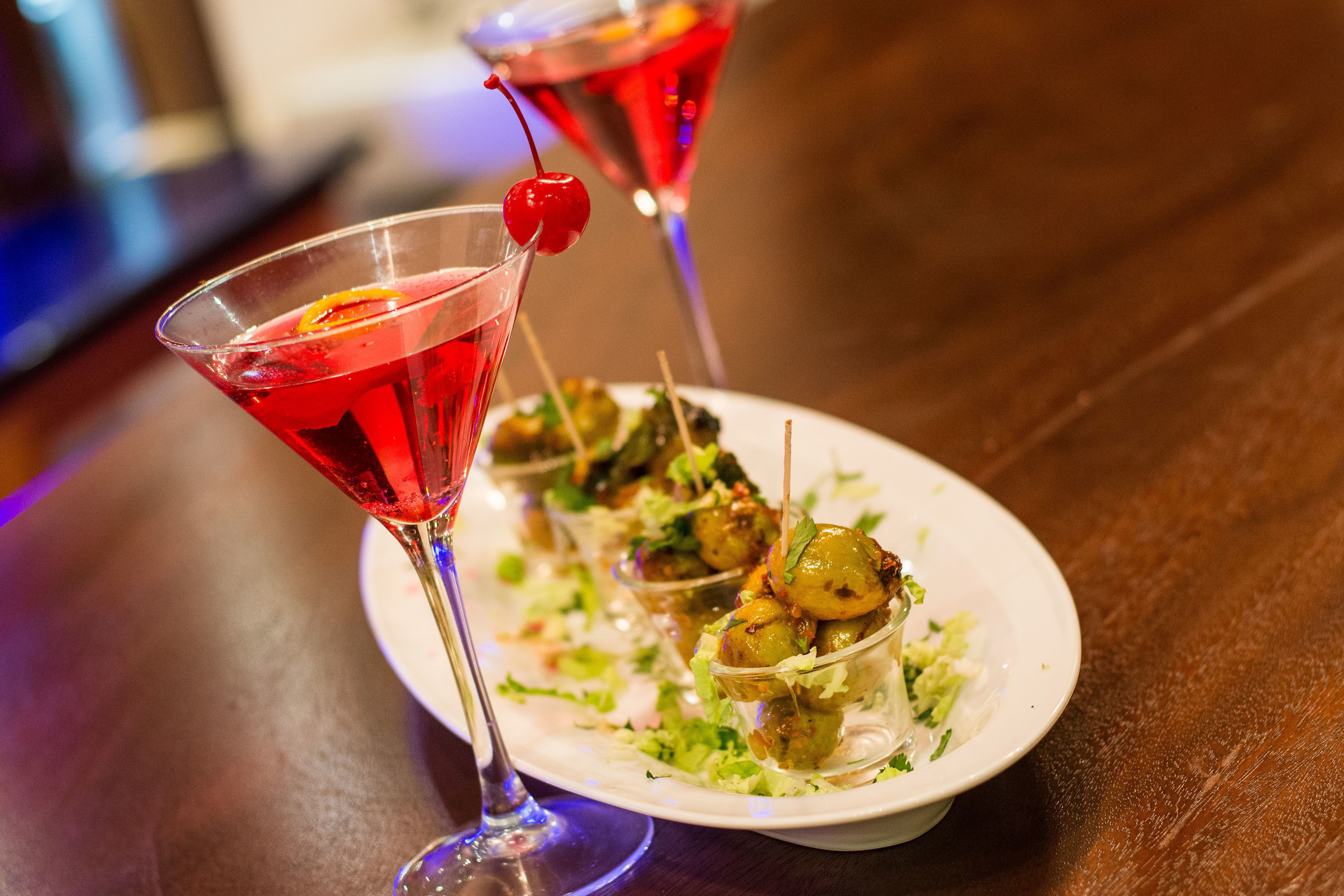 Un verre à martini, avec une cerise, posé sur une assiette blanche contenant des amuse-gueules.