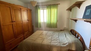 A bedroom with a bed, wooden wardrobe, and a window with green curtains. - Rent cozy apartment (Nivar)