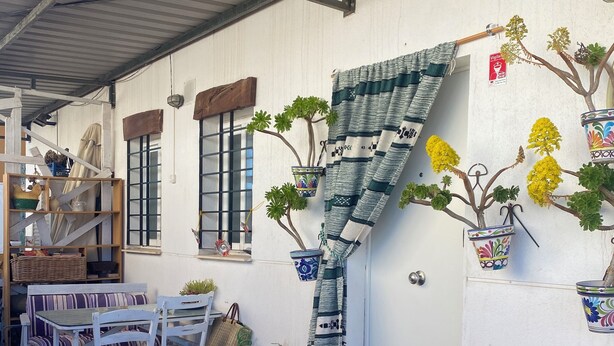 A rustic outdoor seating area with white wooden chairs and a table, a small garden with potted plants, and a staircase leading to an upper level. - Rent cozy apartment (Nivar)