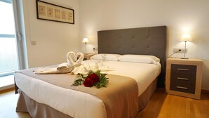 A neatly made bed with a heart-shaped towel arrangement, a bedside lamp, and a small cabinet. - Apartment in front of Fira Gran Via (Hospitalet de Llobregat - Barcelona)